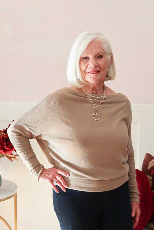 Woman wearing a truffle Kira knit top with boat neckline and relaxed dolman sleeves, styled with dark denim jeans.