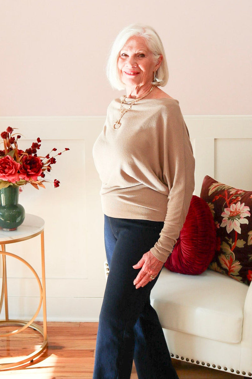 Woman wearing a truffle Kira knit top with boat neckline and relaxed dolman sleeves, styled with dark denim jeans. 