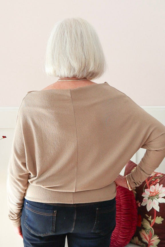 Woman wearing a truffle Kira knit top with boat neckline and relaxed dolman sleeves, styled with dark denim jeans.